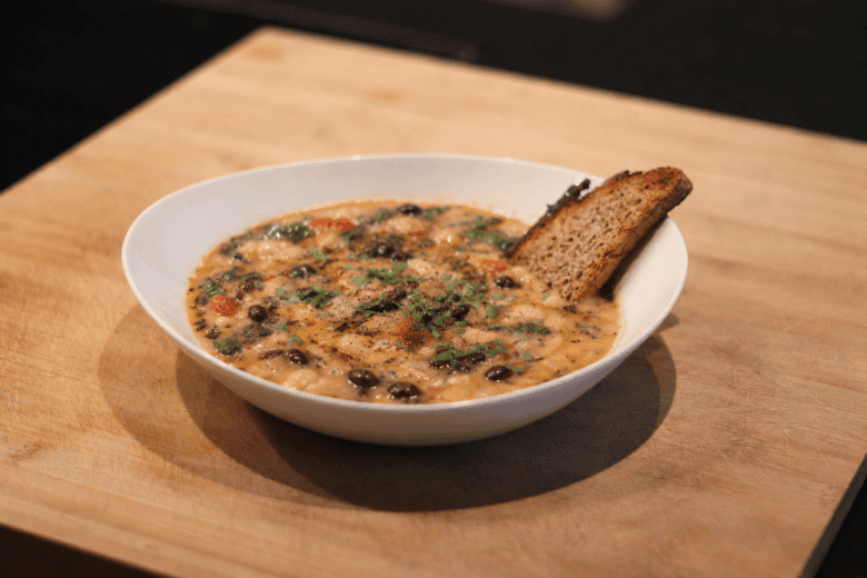 Herbstliche Bohnensuppe in Schüssel mit Brotkruste.