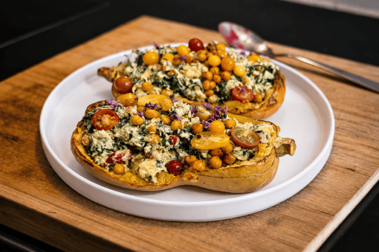Gefüllter Kürbis mit Grünkohl, Kichererbsen und Ricotta auf weißem Teller.