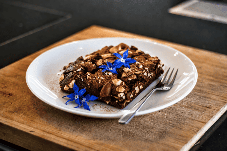 Veganer Rote Beete Brownie mit Nusstopping auf weißem Teller.