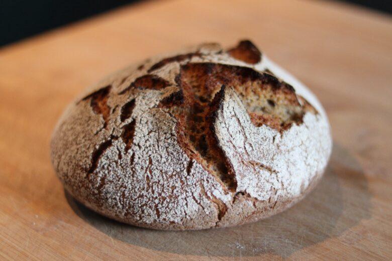 A round loaf of rustic, crusty bread with a cracked golden-brown surface sits on a wooden cutting board.