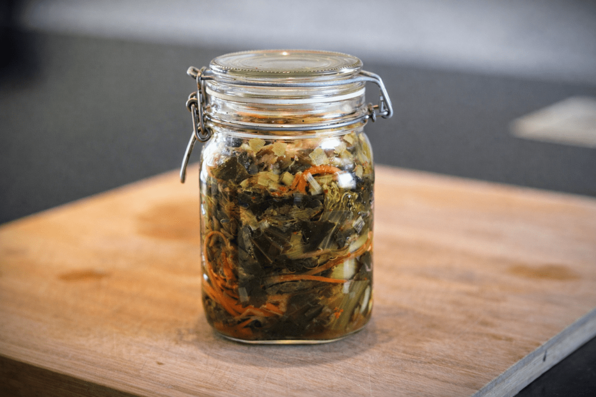 Bärlauchkimchi in einem Glas auf einem Holzbrett.