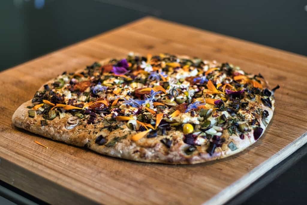 Gemüsepizza mit buntem Gemüse auf Holzbrett.