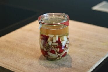 Fermentierter Bierrettich in einem Glas mit Knoblauch und Gewürzen.