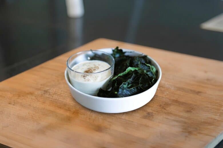 Palmkohlchips mit Cashew-Dip serviert auf Holzbrett.